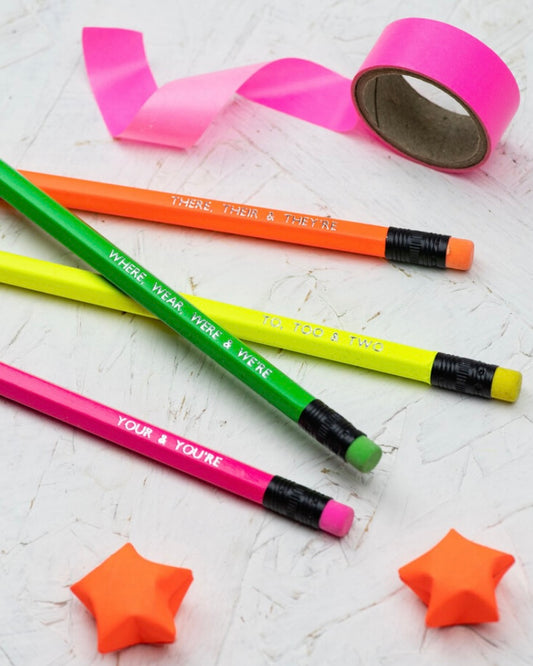 Colourful pencils with grammar related text and origami stars on a textured surface with pink tape