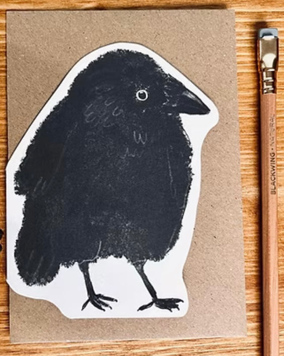 Shaped card with black Jackdaw illustration on a brown envelope, with a pencil on a wooden surface