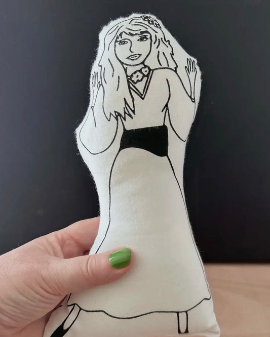 Hand holding a plush toy with a black and white outline of Kate Bush against a dark background