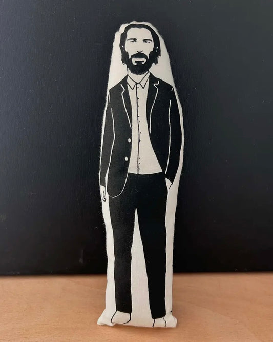 Plush toy of Keanu Reeves wearing a suit on a black background