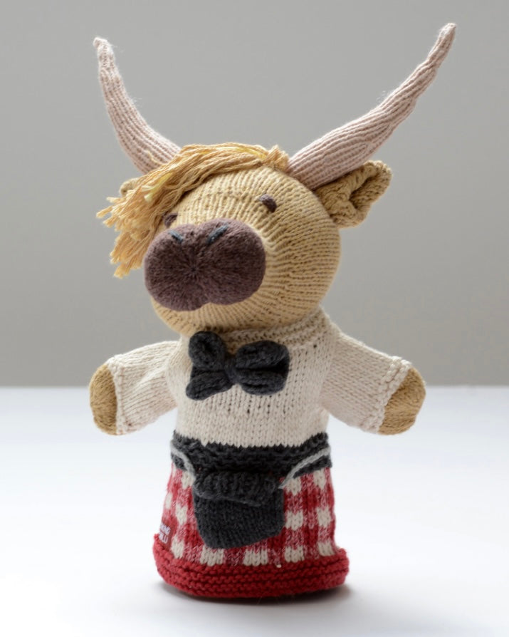 Knitted hand puppet toy highland cow with a bow tie and red tartan kilt,  on a light background