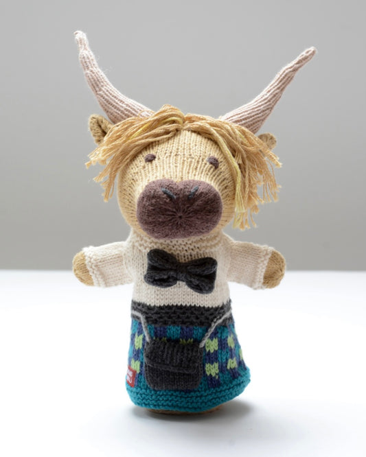 Knitted puppet toy highland cow for little hands with a bow tie and blue and green kilt, on a light background
