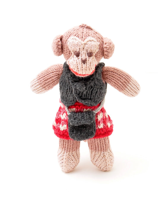 A hand-knit plush monkey toy wearing a dark grey vest, red and white patterned kilt, and a red collar, set against a plain white background.