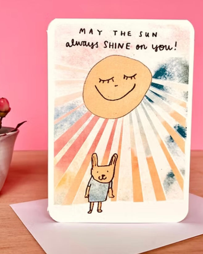 Card with a sun and rabbit illustration and text 'May the sun always shine on you!' on an envelope.