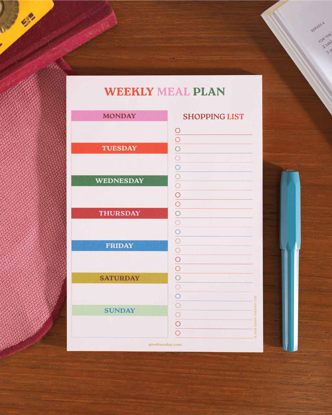 Weekly meal plan and shopping list on a wooden surface with a pen.