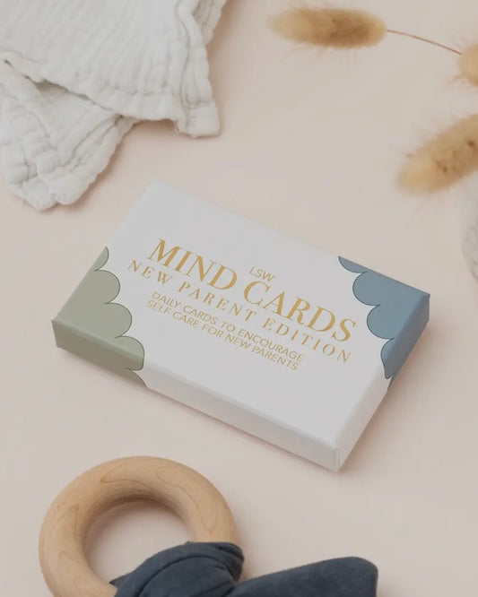 Box (top) of 'Mind Cards' for new parents on a soft surface with baby items.