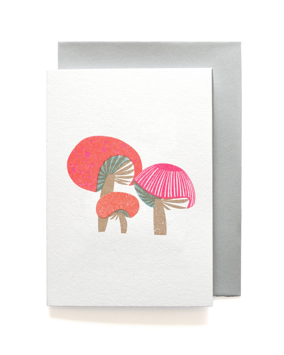 A white greeting card featuring a minimalist illustration of two pink and coral mushrooms, shown with a silver-gray envelope behind it on a clean white background.
