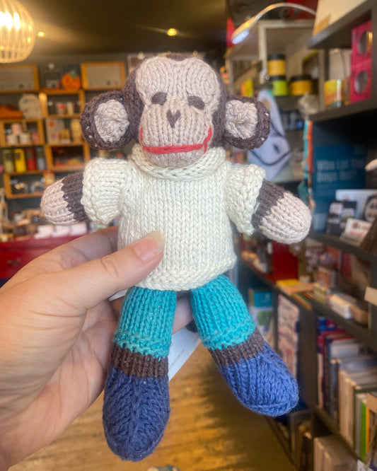 Knitted monkey toy held in a hand, with a shop background.