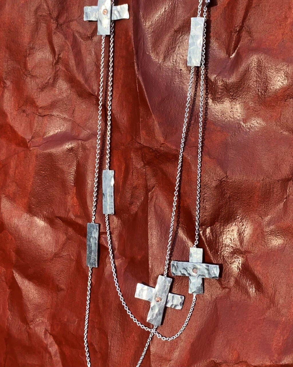 Silver cross and bar necklace on a textured red surface