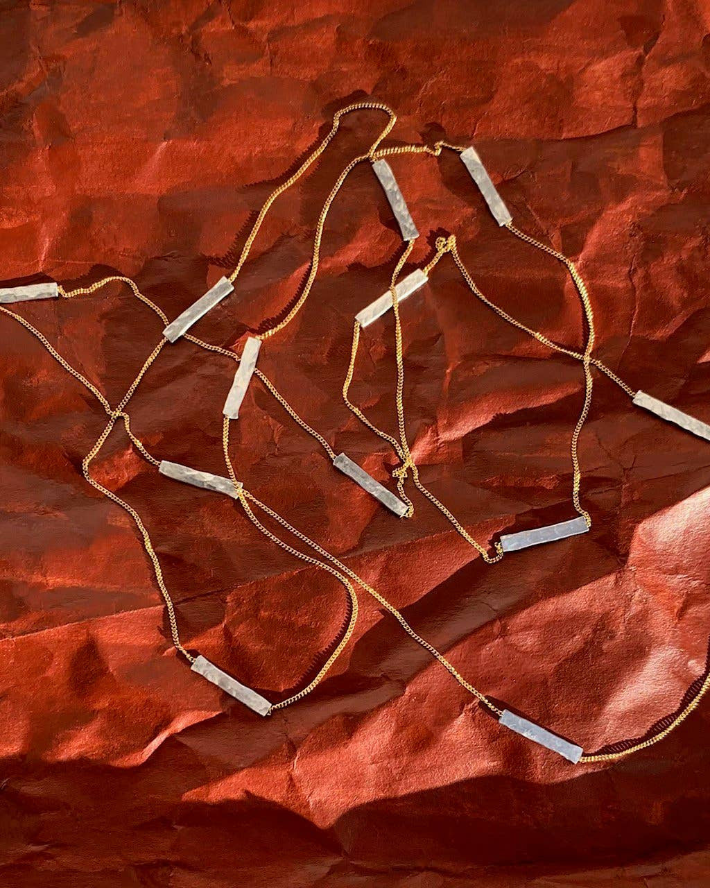 Necklace with bar pendants on a textured red fabric background
