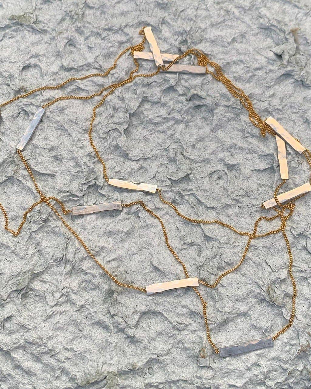 Gold chain necklace with silver sections on a textured stone surface