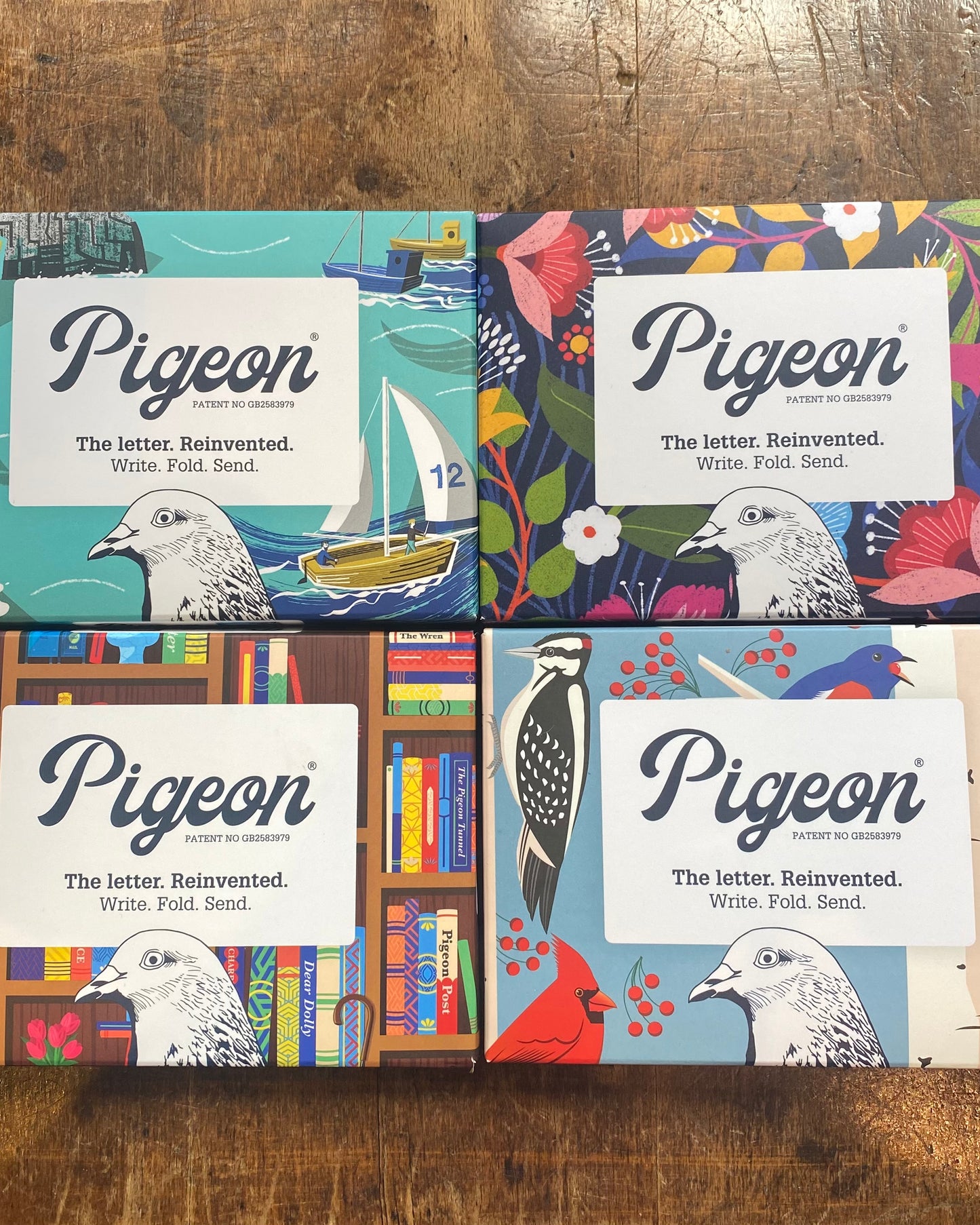 Four Pigeon 'The Letter, Reinvented.' writing paper gift boxes arranged in a 2x2 grid on a wooden tabletop.