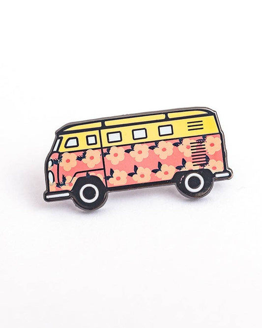 A small enamel pin shaped like a retro campervan, featuring a yellow upper section and a pink floral patterned lower body, outlined in black metal on a white background.