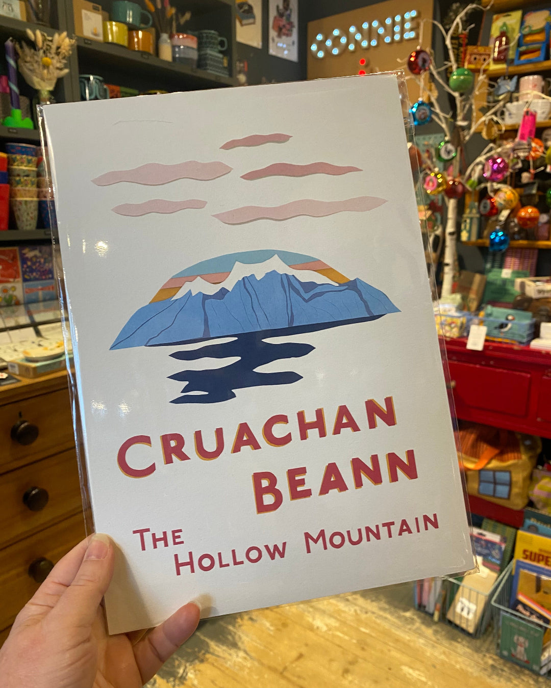 Print of mountain titled 'Cruachan Beann: The Hollow Mountain' held in a store setting.
