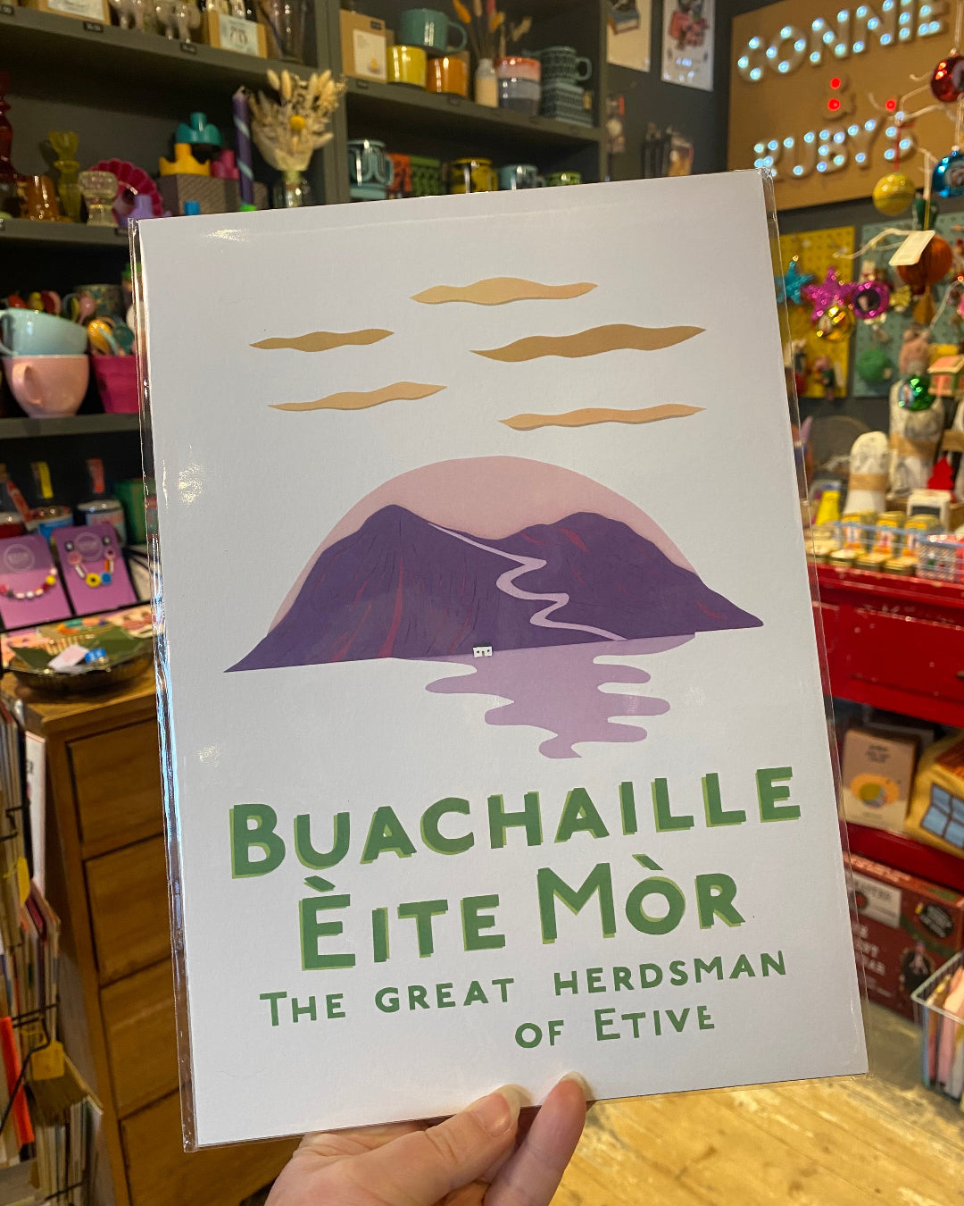 Poster with mountain design and Gaelic text held in a store setting