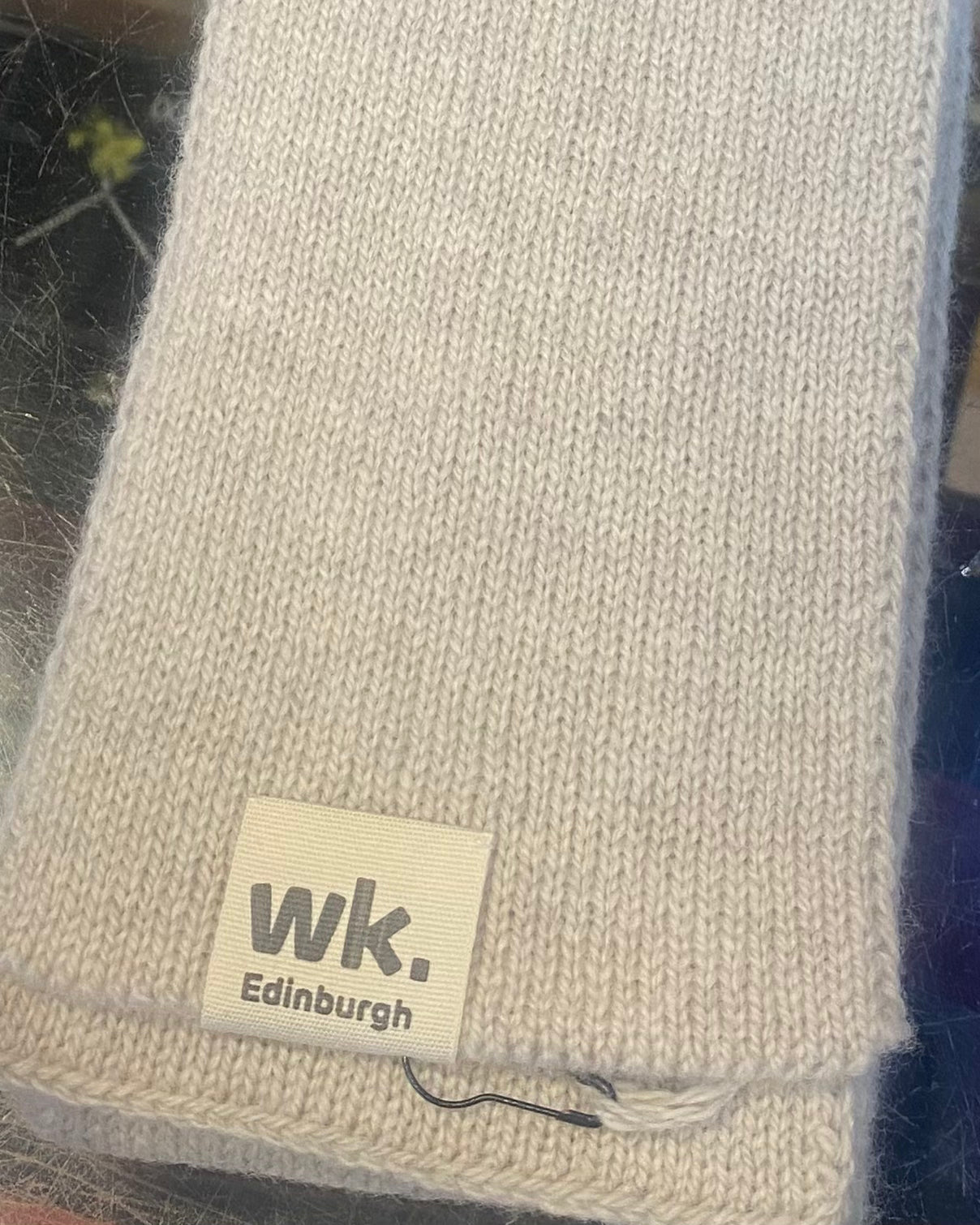 Beige knitted wool scarf with a 'wk. Edinburgh' label on a dark background