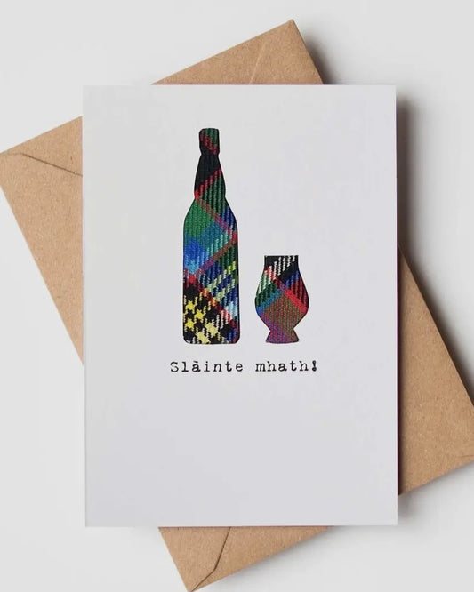 White greeting card with real tartan inset, showing a whisky bottle and glass, with the words Slainte Meath! underneath, with a brown kraft envelope 