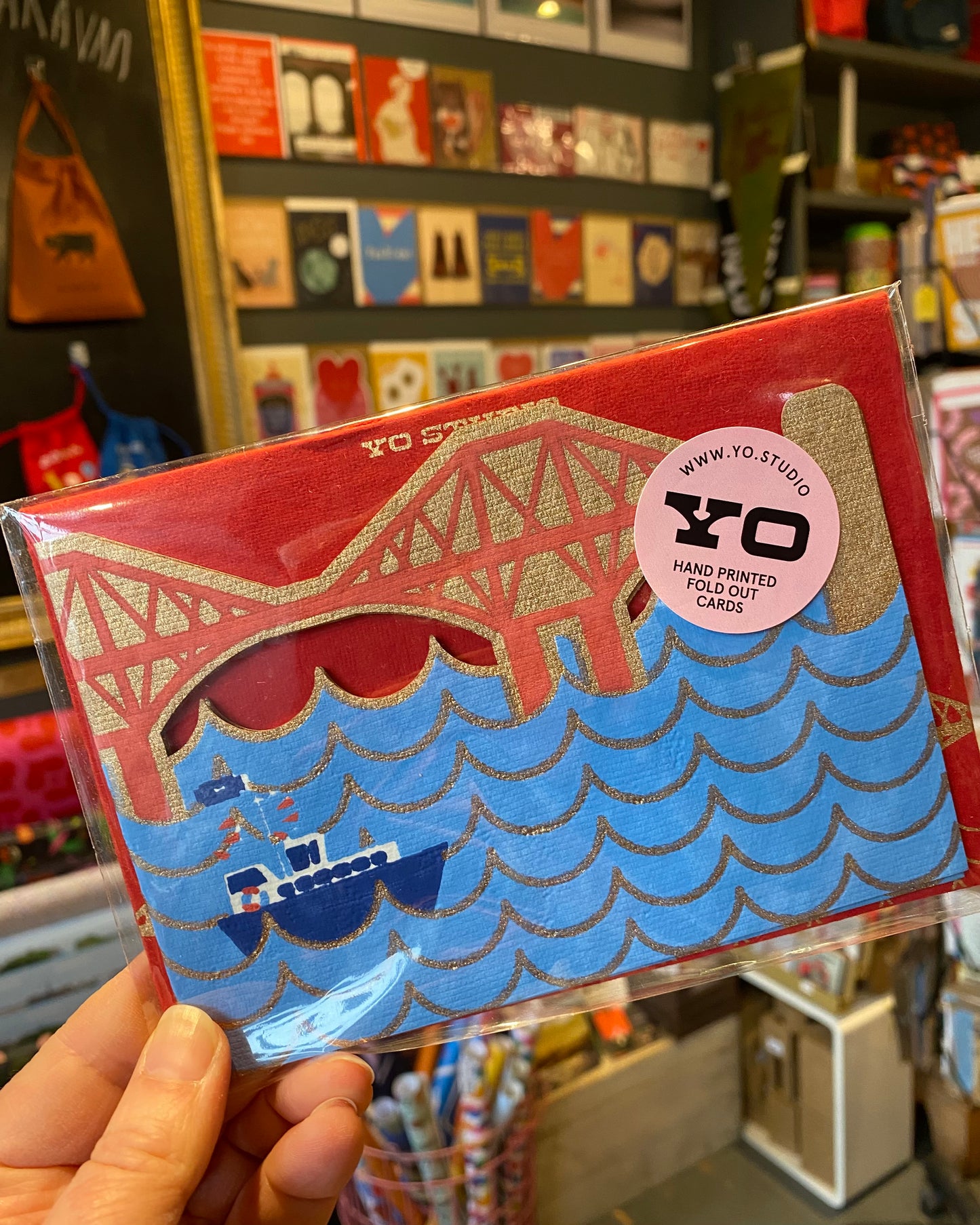 Packaged card with a Forth bridge design held by a hand in a store setting