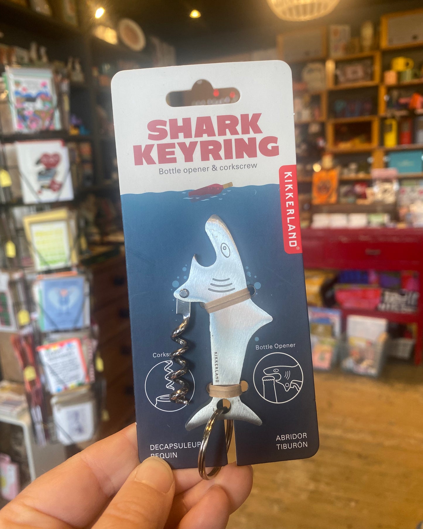 Shark keyring with packaging held in front of a store shelf.
