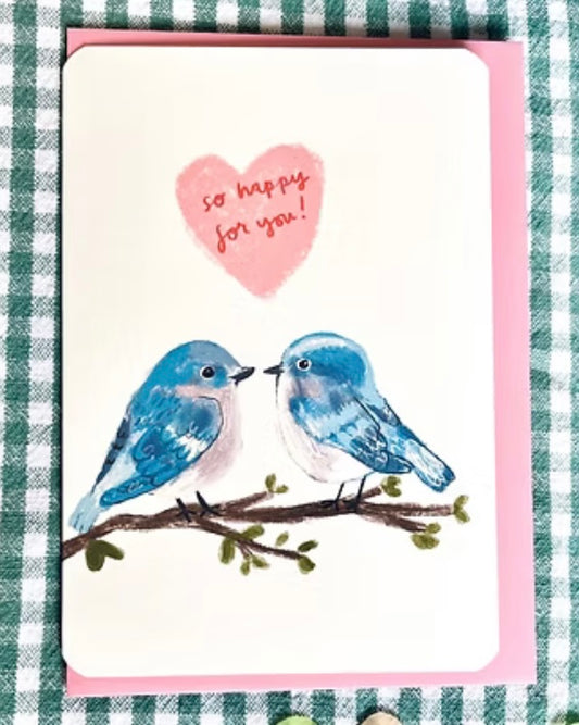 Card with two blue birds on a branch and a pink heart with text, on a green and white checkered background.