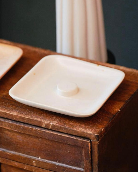 White ceramic square incense holder dish on a wooden surface with a blurred background