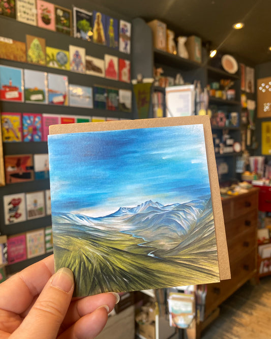 Small square greetings card featuring  a painting of a mountain landscape - Lochnagar - in a store setting.