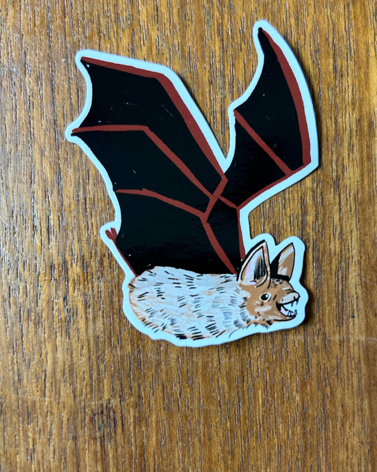 Sticker of a bat wings and furry body, on a wooden surface