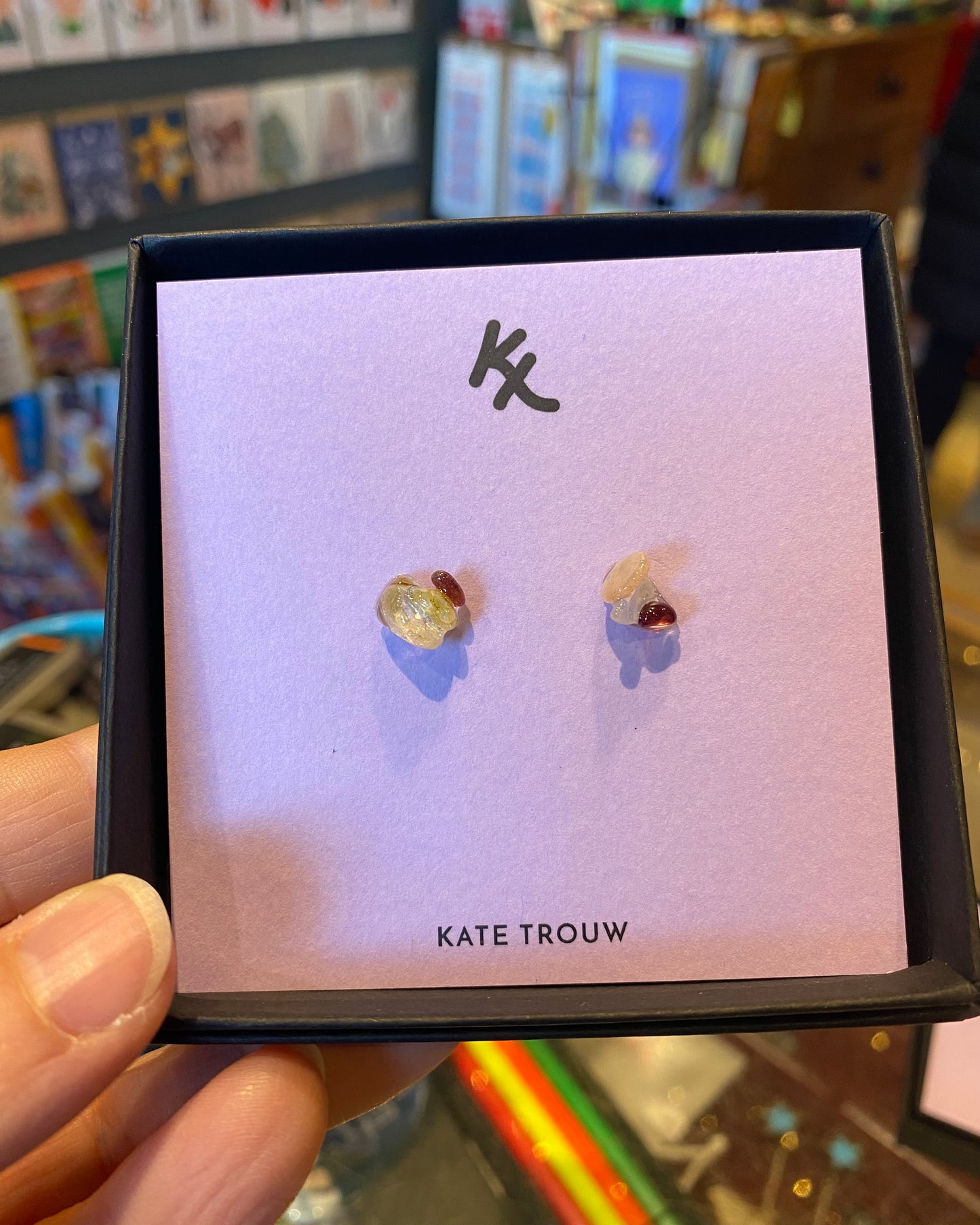 Pair of glass and gem earrings on a Kate Trouw card held by a person.