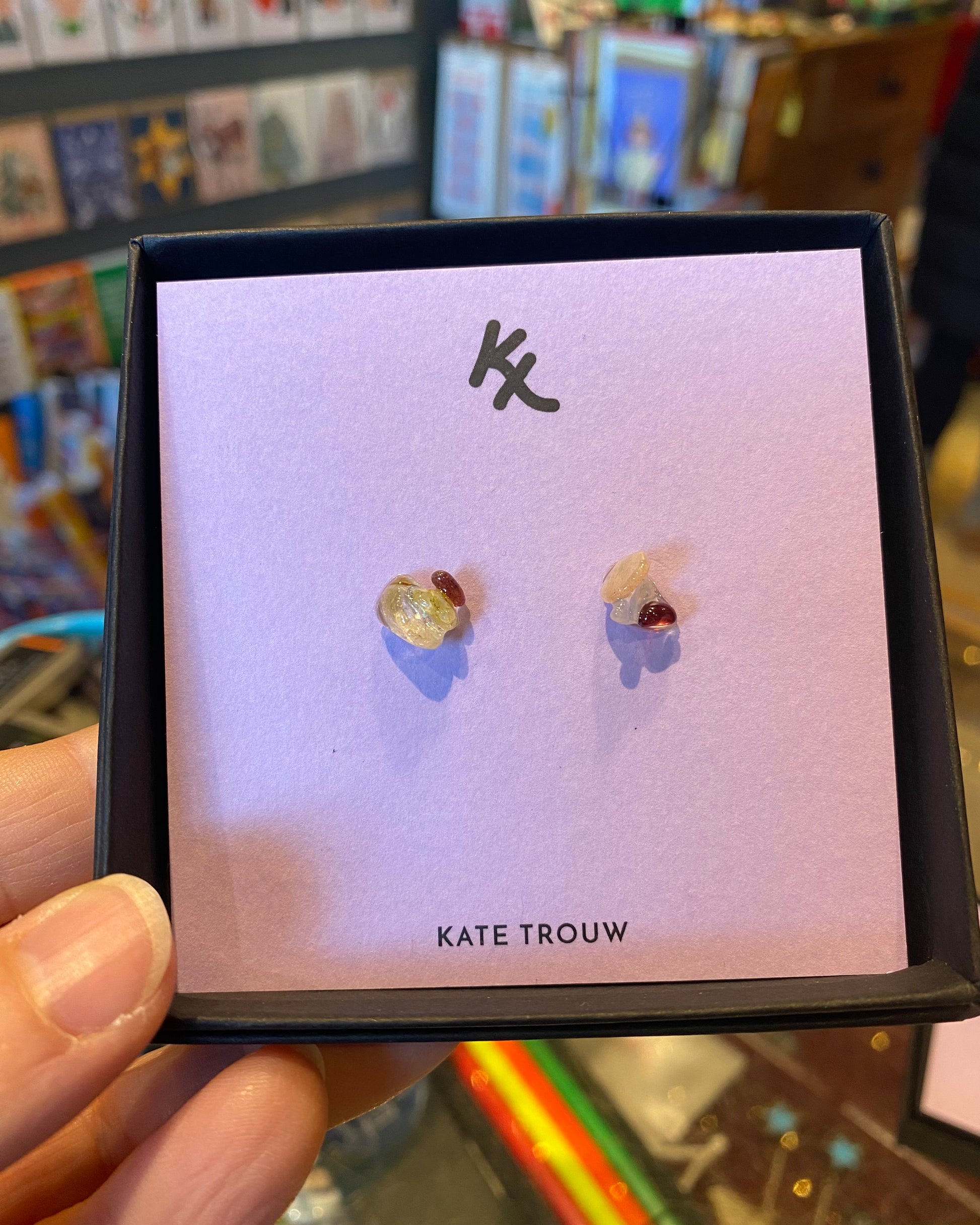 Pair of glass and gem earrings on a Kate Trouw card held by a person.