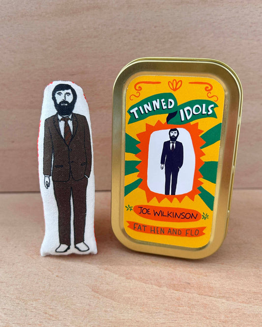 Tinned Idol figure and packaging on a wooden surface