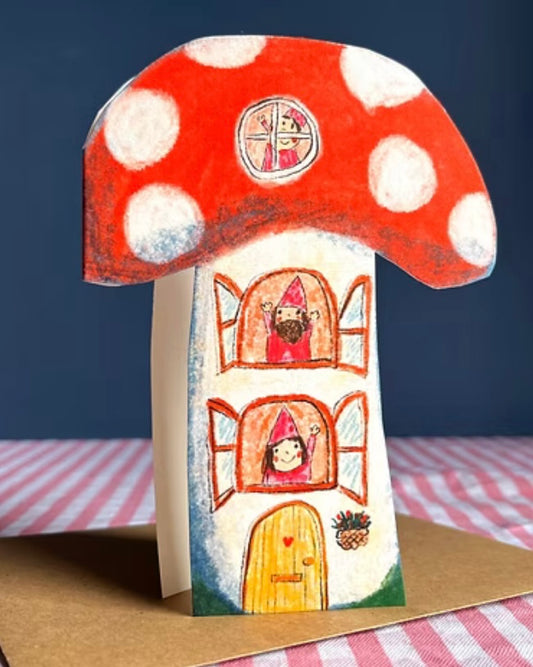 Mushroom-shaped card with polka dot top on a brown kraft envelope, sitting upright on a checkered tablecloth.