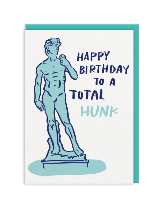 Birthday card with statue illustration and humorous text ‘Happy Birthday to a total hunk’, with a teal envelope on a white background