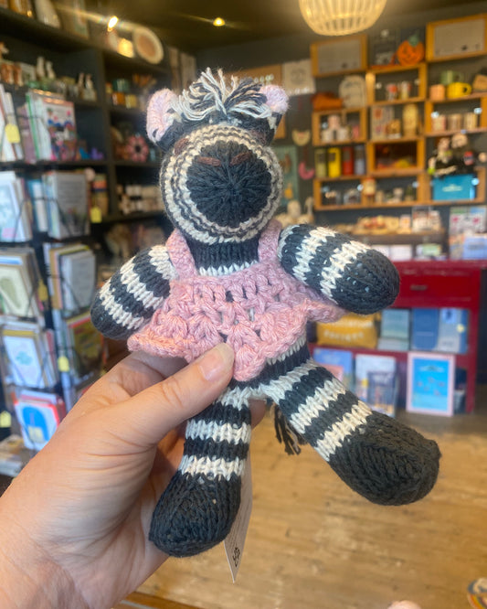 Handmade crochet zebra toy in a pink dress, held in a store setting.